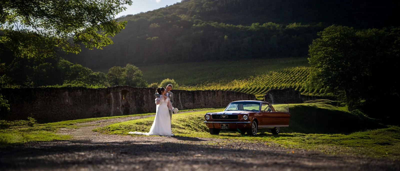 Un couple de jeunes mariés près d'une voiture ancienne, dans les vignes de la région